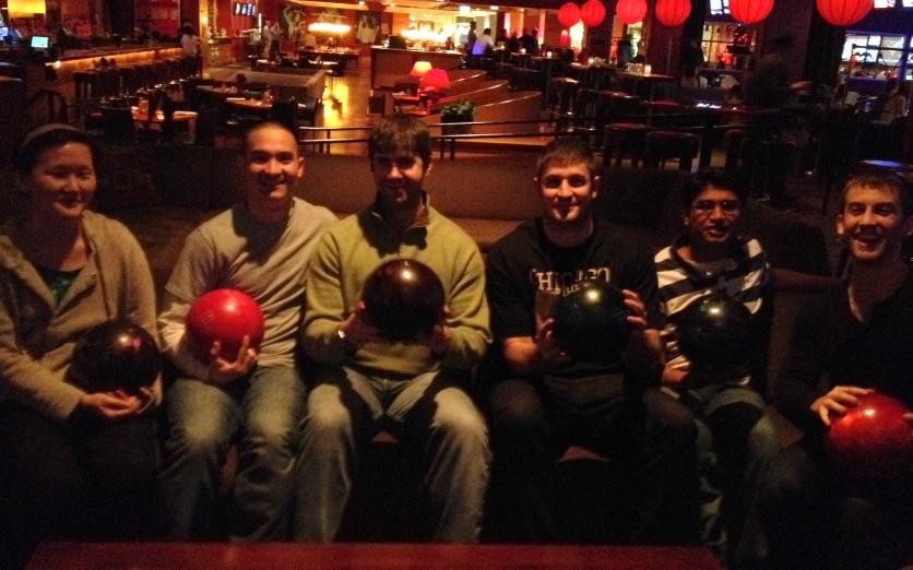 Members posing with bowling balls in a dim bowling alley